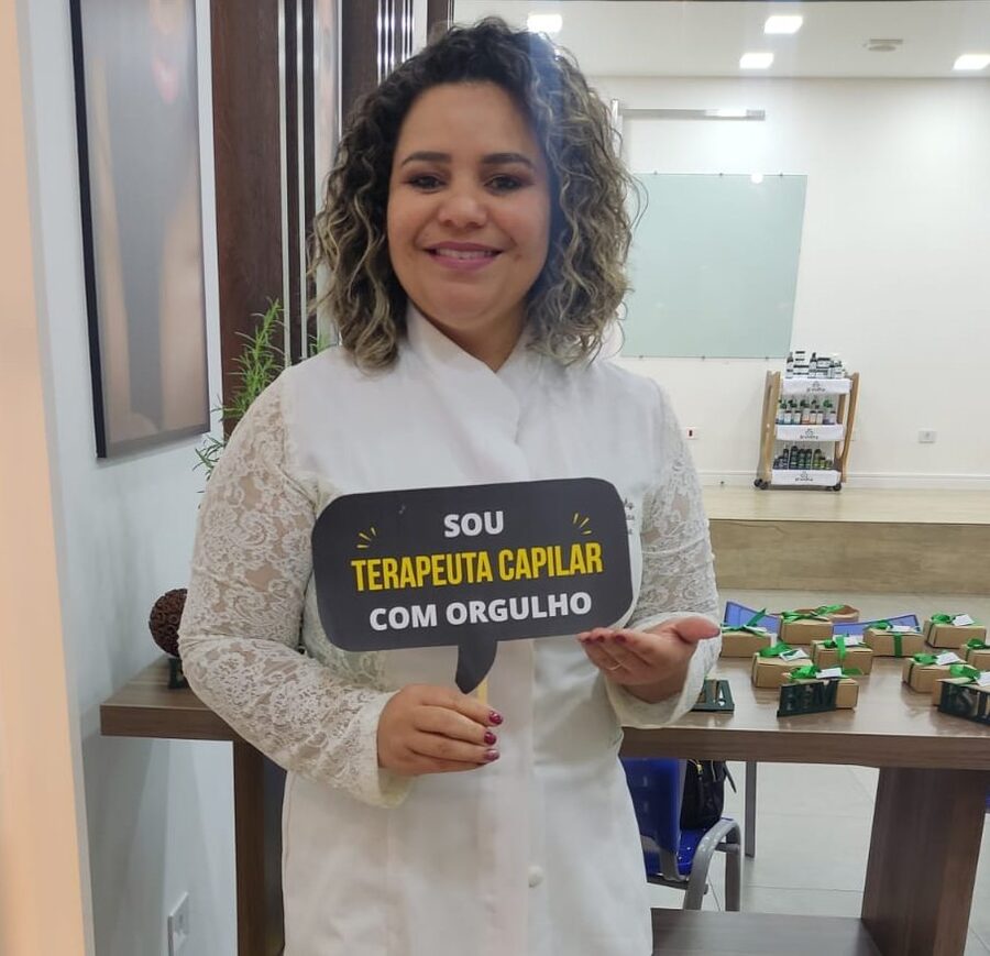 Lucinéia Sabina no estúdio, segurando uma placa com os dizeres Sou terapeuta capilar com orgulho
